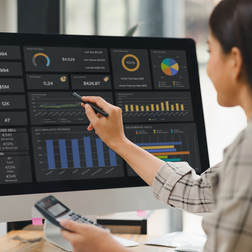 Kobieta wskazująca rysikiem wykresy sprzedaży i przychodów na komputerze w nowoczesnym biurze