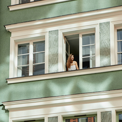 Gość w otwartym oknie butikowego hotelu nad parterową kawiarnią, zielona elewacja, poranne słońce i relaksująca atmosfera