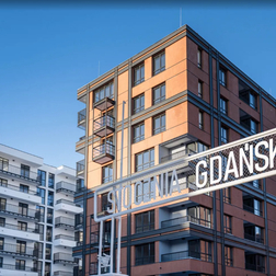 Nowoczesne apartamentowce z balkonami i dużymi oknami, ceglana i biała elewacja, metalowy szyld „GDAŃSKA”.