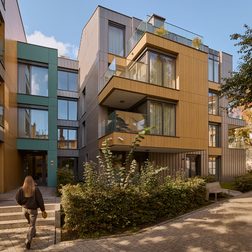 Nowoczesny butikowy hotel z drewnianą elewacją, przeszklonymi balkonami, zielonym dziedzińcem i gościem idącym do wejścia