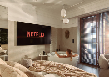 Luksusowy apartament z wygodnym łóżkiem i wolnostojącą wanną; gość relaksuje się, oglądając Netflix, zdobiony sufit i słoneczny balkon.
