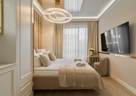Elegancki beżowy pokój hotelowy z łóżkiem king-size, pikowaną pościelą, okrągłym żyrandolem, telewizorem i ręcznikami