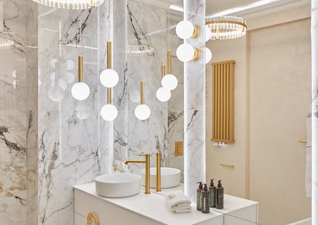 Luksusowa łazienka z marmurowymi ścianami, wolnostojącą wanną, złotymi armaturami, podwójnymi umywalkami i kosmetykami