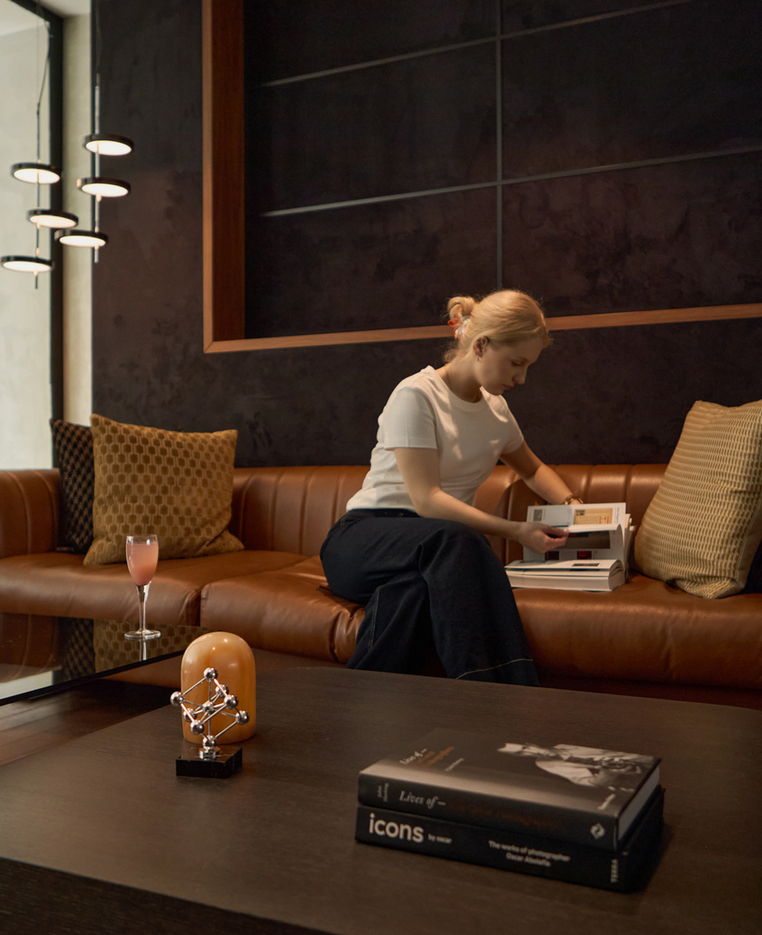 Gość na skórzanej sofie w stylowym lobby hotelu, przegląda broszurę obok koktajlu na szklanym stoliku