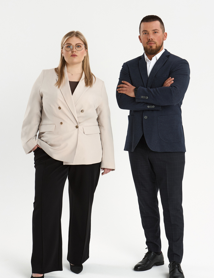Dwójka pracowników hotelu w eleganckich marynarkach stoi pewnie na białym tle.