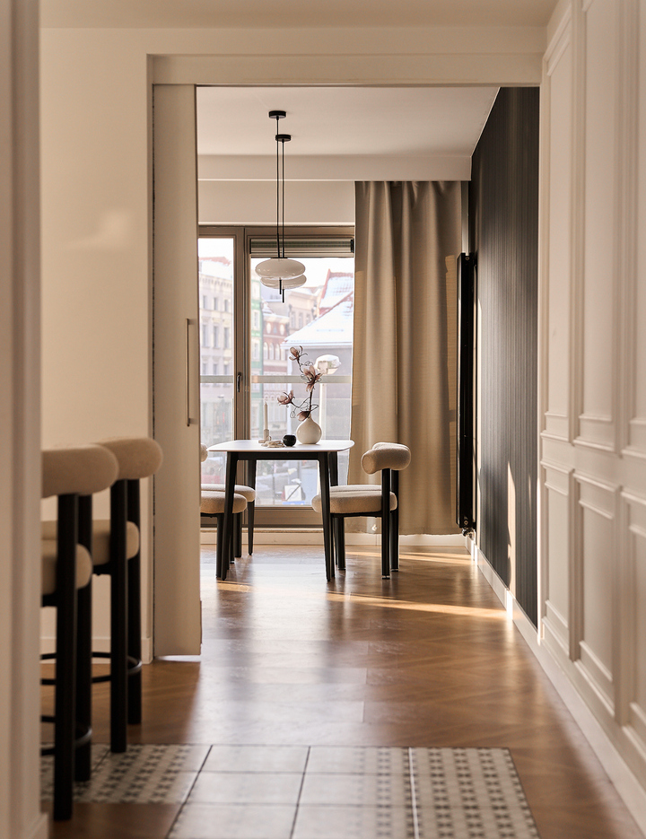 Przytulny kącik jadalny w hotelu butikowym: okrągły stół, tapicerowane krzesła, lampa wisząca, wazon z kwiatami i widok na miasto