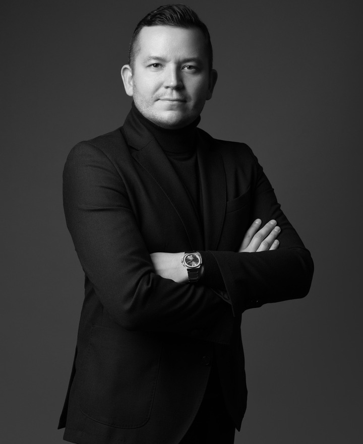 Portret menedżera hotelu w czarnym garniturze i golfie, ramiona skrzyżowane, pewny wyraz, studyjne oświetlenie