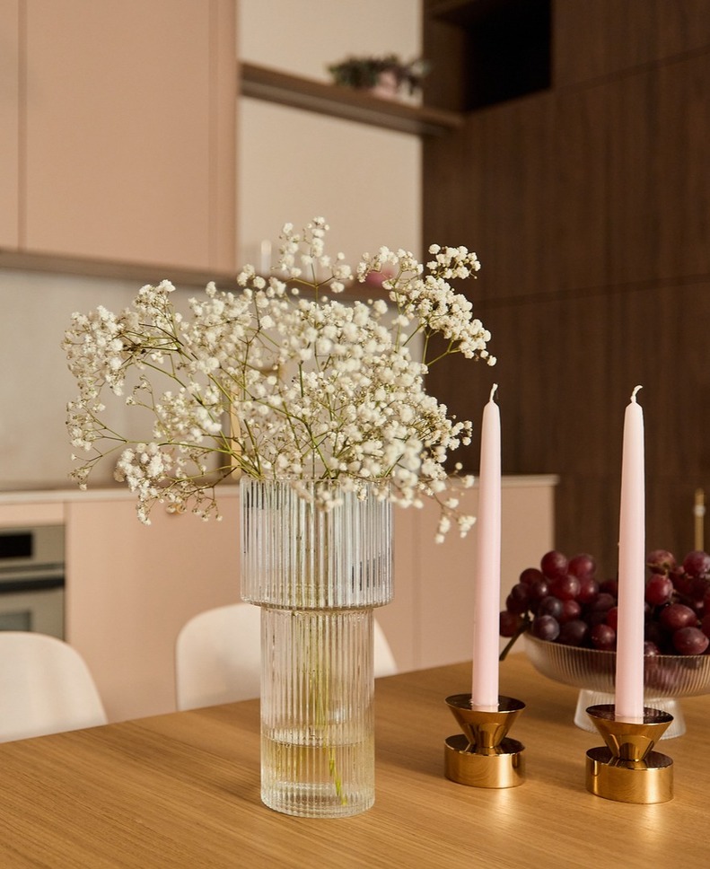 Nowoczesny stół w kuchni z przezroczystym wazonem gipsówki, różowymi świecami w złotych świecznikach i misą czerwonych winogron.