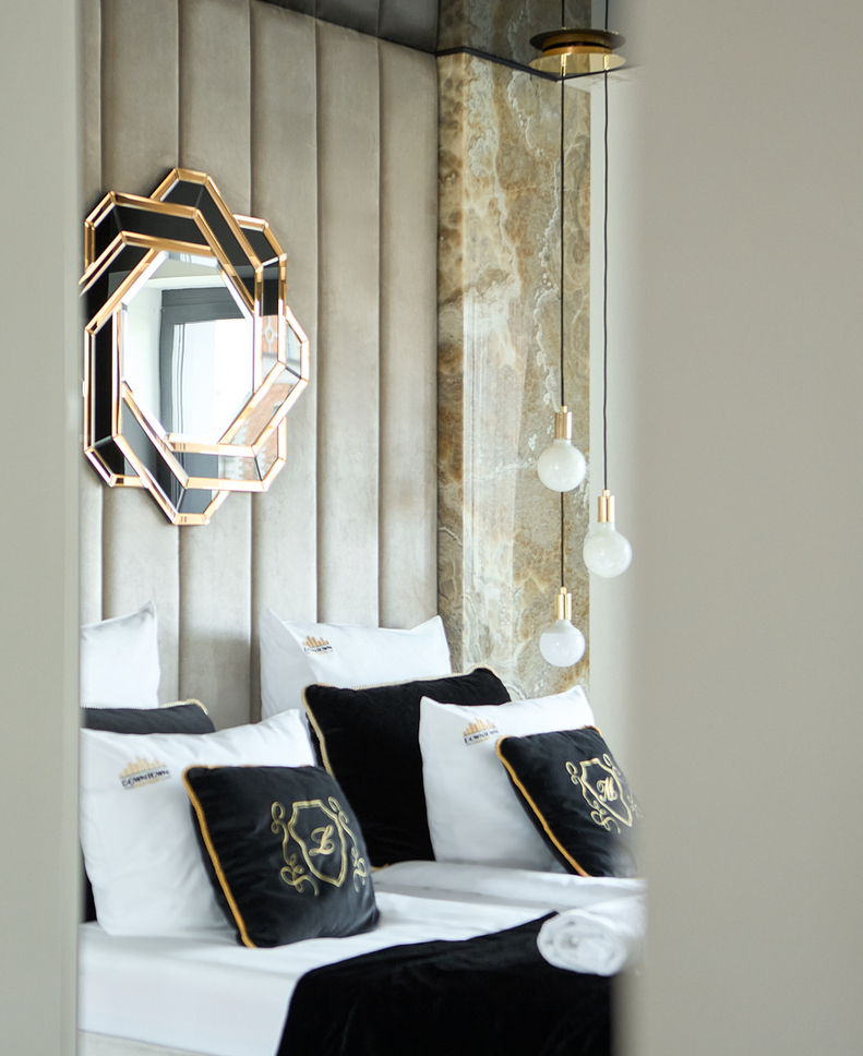 Luksusowe łóżko z wysokim zagłówkiem, geometryczne lustro, marmurowy akcent, czarne poduszki w welurze, lampy wiszące.