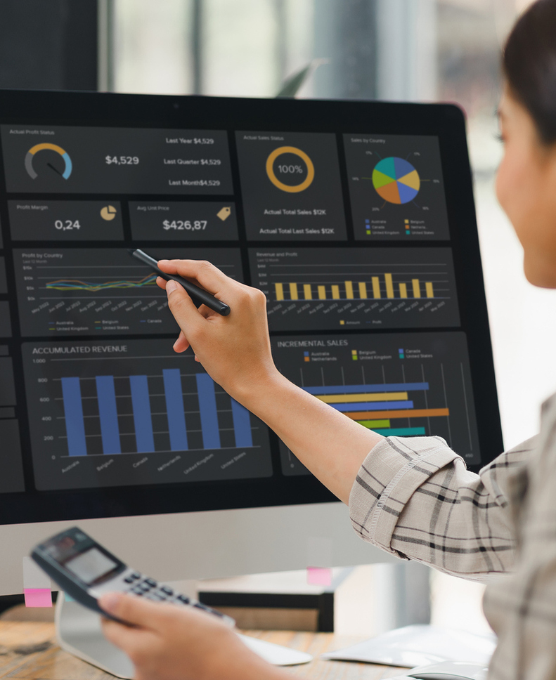 Kobieta wskazująca rysikiem wykresy sprzedaży i przychodów na komputerze w nowoczesnym biurze