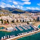 Marina con yacht, spiaggia sabbiosa e hotel sul lungomare, città con suggestive montagne sullo sfondo