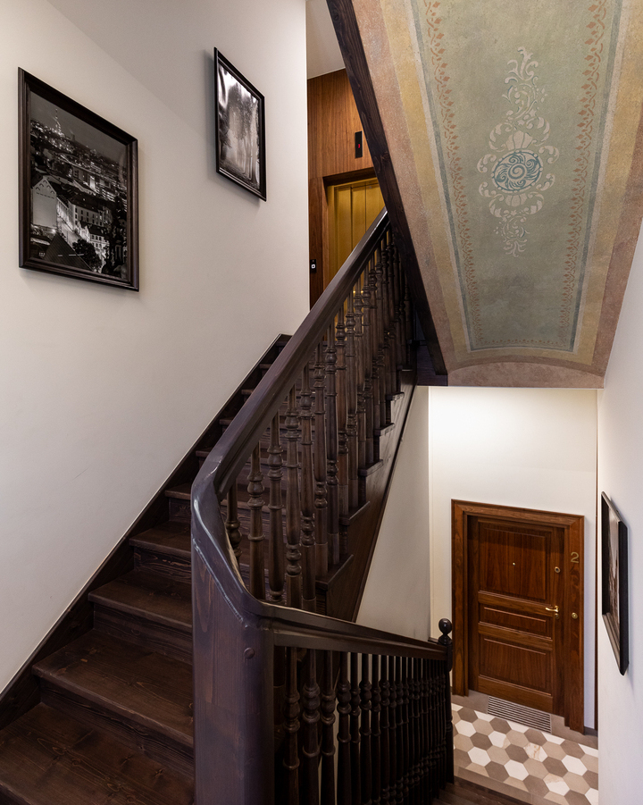 Kręte ciemne drewniane schody pod ozdobnym malowanym sufitem w butikowym hotelu, geometryczna podłoga, zdjęcia w ramkach i drzwi pokoju nr 2.