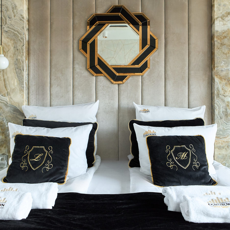 Luksusowe dwa łóżka z czarno-złotymi poduszkami, białą pościelą, marmurowymi panelami, wiszącymi kulistymi lampami i geometrycznym lustrem