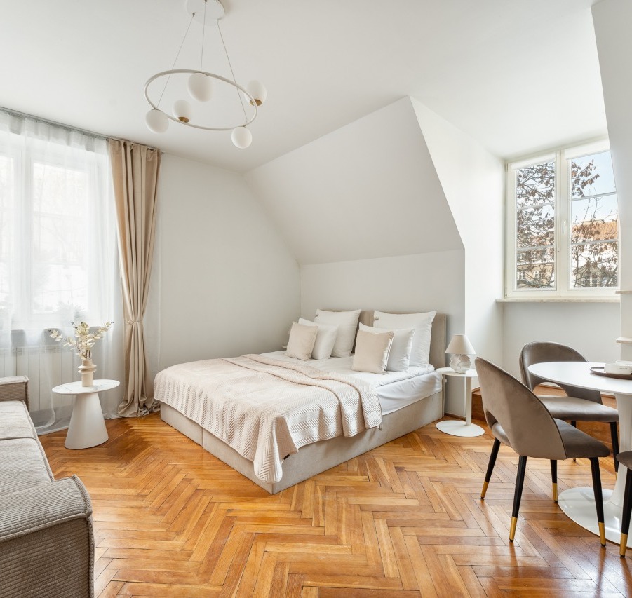 Jasne, nowoczesne studio z dwuosobowym łóżkiem, sofą, jadalnią, parkietem w jodełkę i stonowaną beżową aranżacją