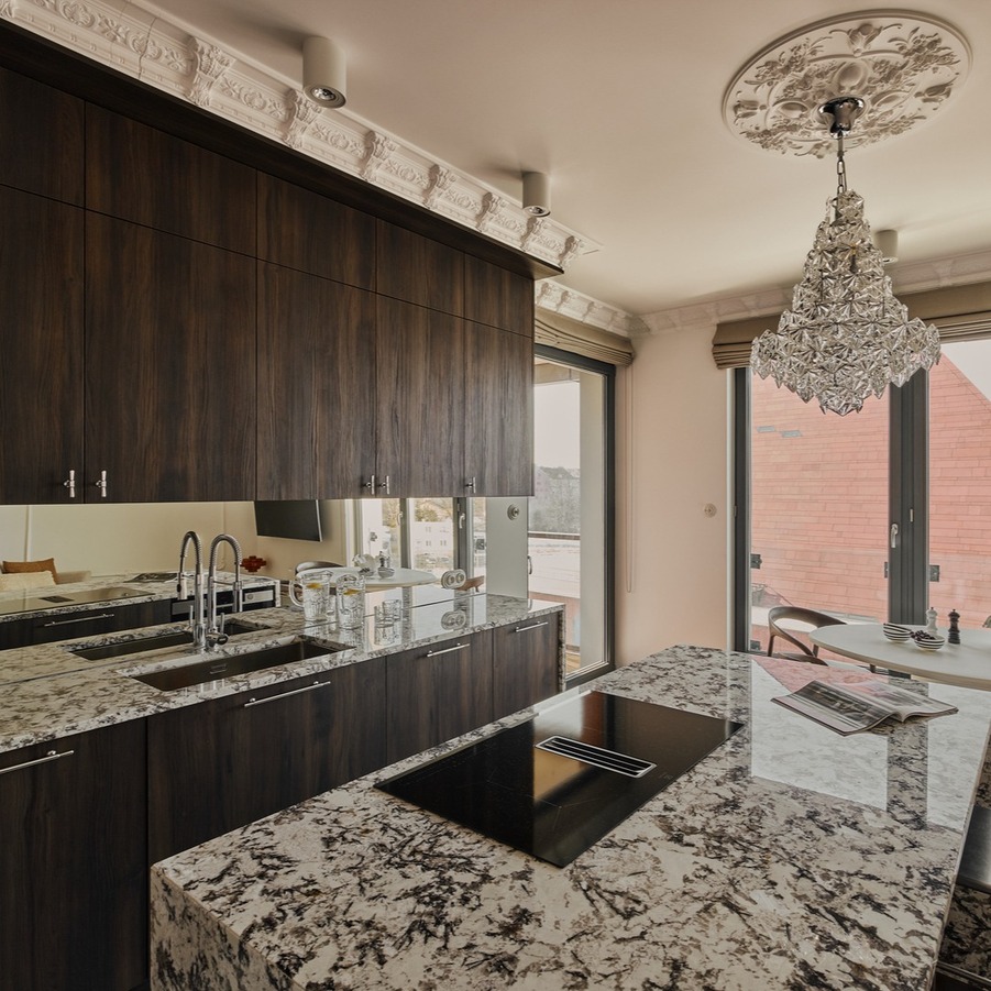 Kuchnia w luksusowym apartamencie z marmurową wyspą i płytą grzewczą, ciemnymi drewnianymi szafkami, kryształowym żyrandolem i widokiem na miasto.