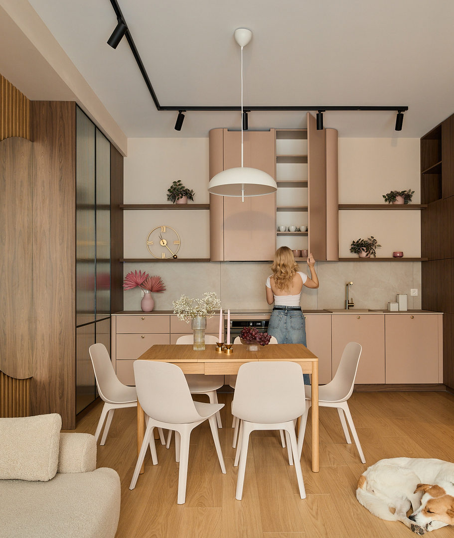 Soggiorno open space con cucina rosa cipria, dettagli in legno, tavolo per sei, lampada sospesa, divano, cane che dorme, ospite al pensile alto.