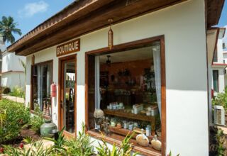 Boutique shop in a tropical hotel setting with white walls, wooden trim, hanging lanterns, and lush garden landscaping