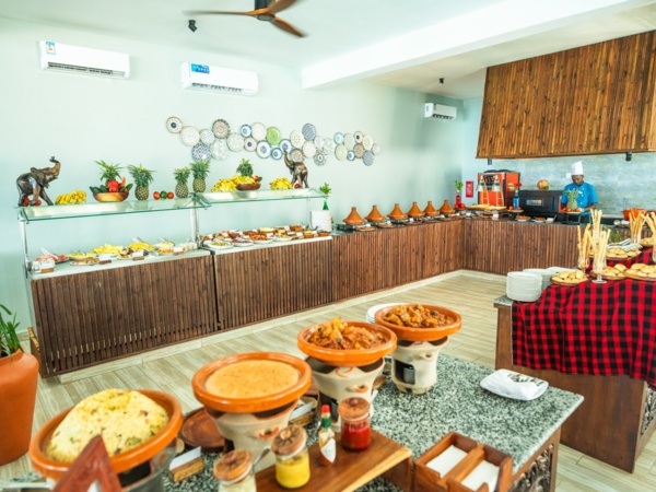 Buffet dining area with traditional dishes in clay pots, fresh fruit displays, warm wooden decor, and a chef preparing meals