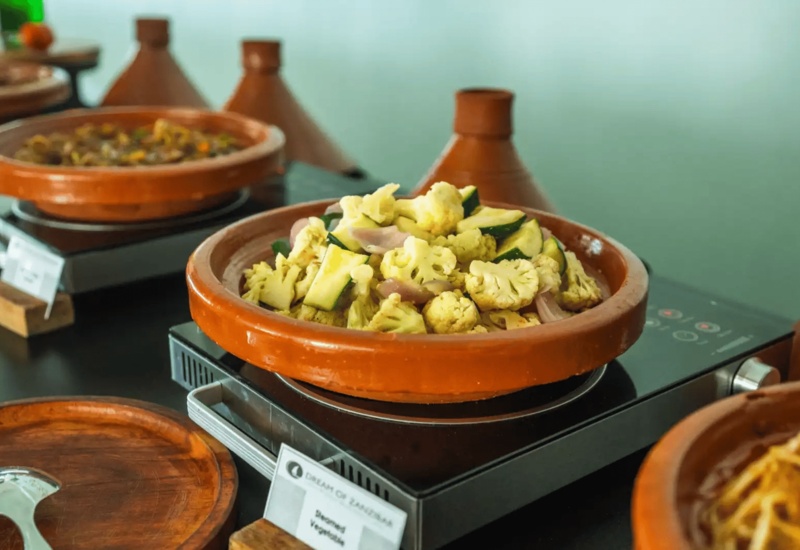 Buffet spread featuring steamed vegetables served in traditional clay tagine pots on warming trays
