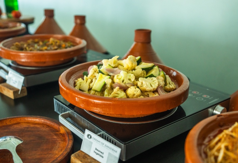 Steamed vegetables served in traditional clay tagine pots on buffet with other dishes in clay pots
