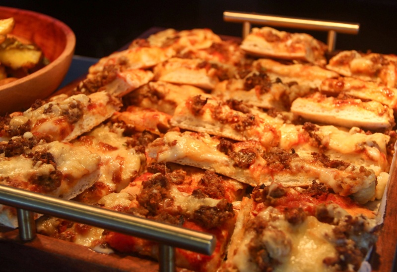 Tray of cheesy meat pizza slices served warm, accompanied by a bowl of seasoned potato wedges, ideal for casual dining