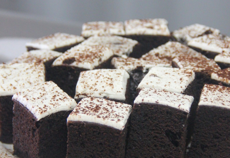 Chocolate cake squares topped with white frosting and a dusting of cocoa powder, served as a dessert option