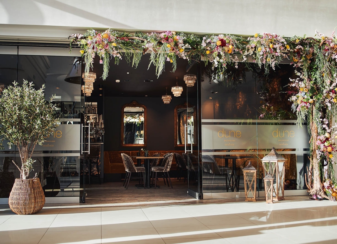 Glass-front brasserie with cascading floral arch, wicker olive tree, lanterns, chandeliers and velvet chairs