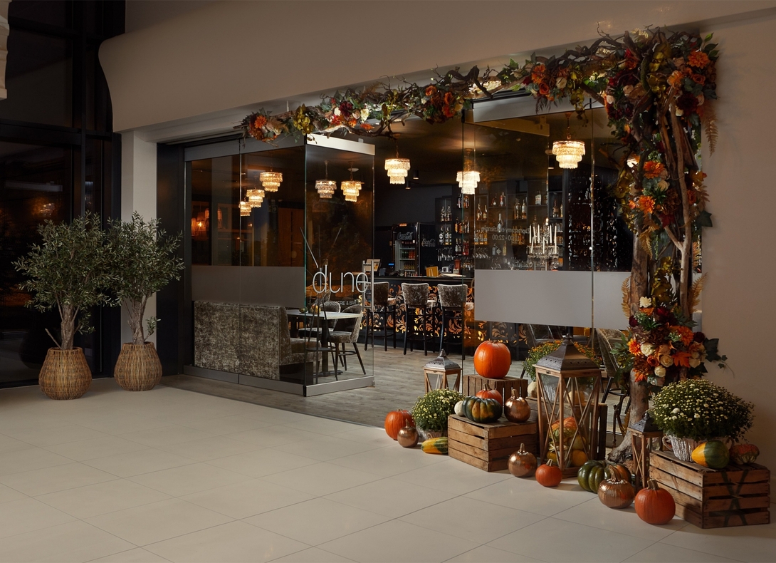 Hotel bar 'dune' with glass façade, crystal chandeliers, cozy seating and autumn décor—pumpkins, lanterns and floral garland.