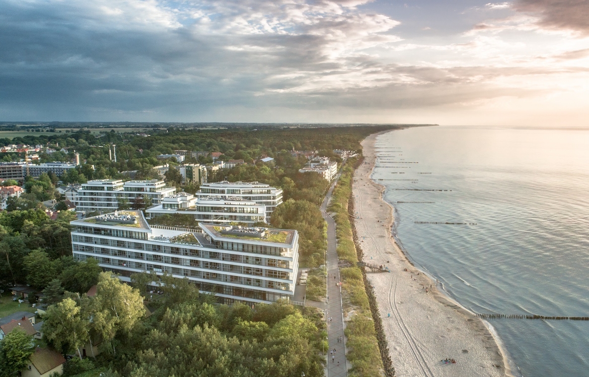 Modern beachfront resort with tiered glass facades, green roofs, seaside promenade and long sandy beach at sunset.