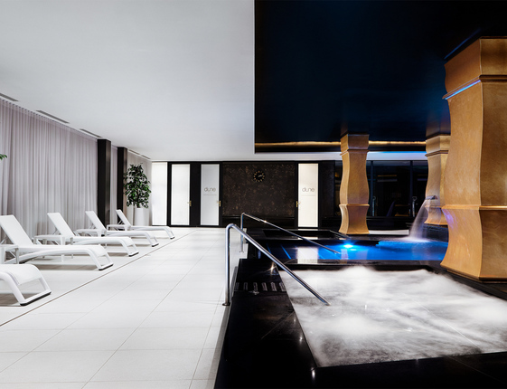 Spa wewnętrzne z bulgoczącym jacuzzi, podświetlonym basenem z kaskadami, złotymi kolumnami i białymi leżakami