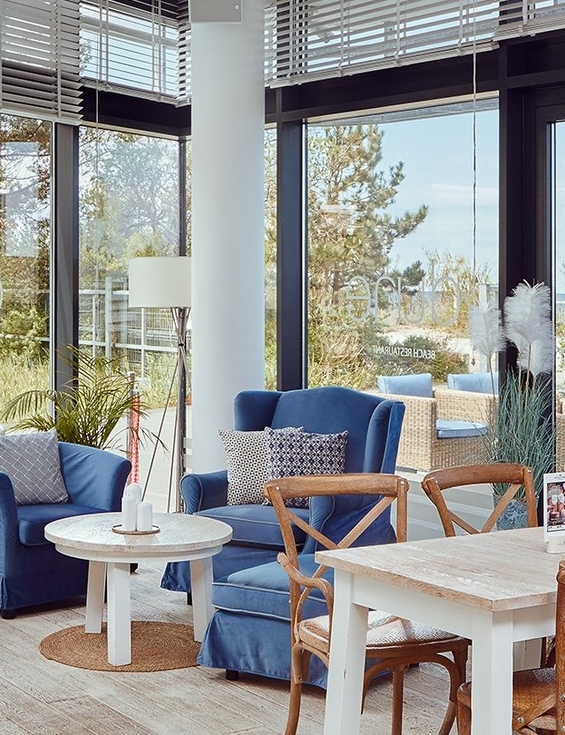 Bright seaside lounge with blue armchairs, wooden tables, rattan terrace seating and Moët & Chandon glass tower.