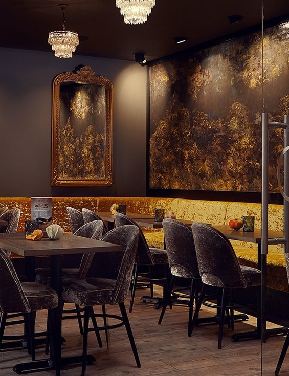 Intimate upscale hotel bar with gold velvet banquette, plush velvet chairs, chandeliers, ornate mirrors and cozy tables