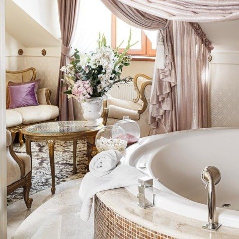 Marble-surrounded round tub with folded white towel, glass jars and floral centerpiece, romantic ambiance.