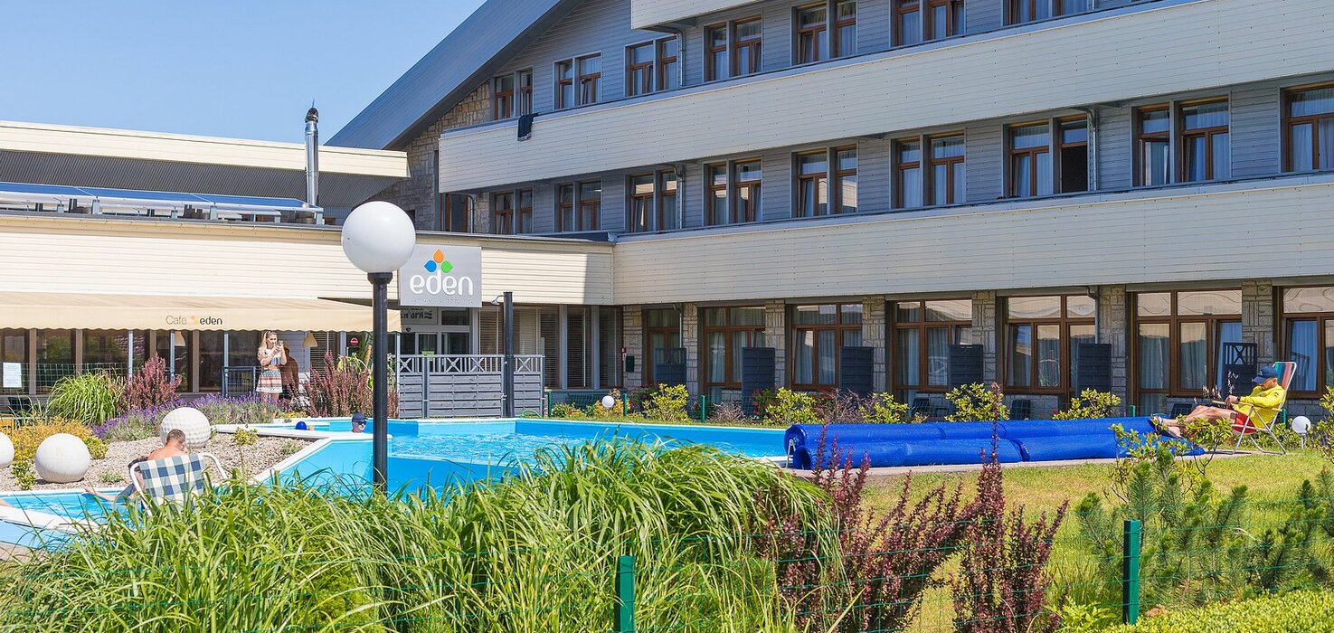 Hotel Eden — outdoor pool, café terrace, loungers and a carefully maintained garden by a modern building.