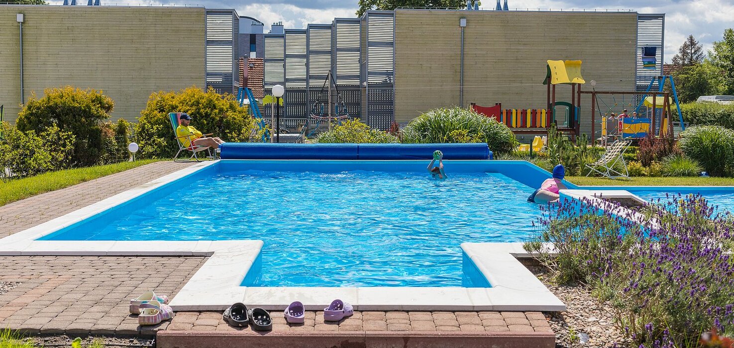 Outdoor hotel pool with loungers, playing children, a playground, lavender beds and relaxation