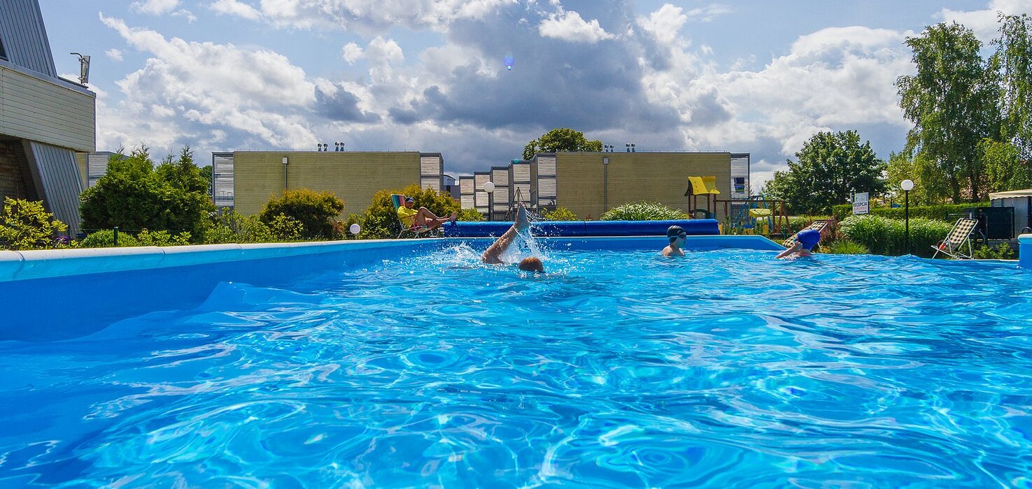Outdoor hotel pool with crystal-blue water, guests swimming, loungers and a playground by the buildings