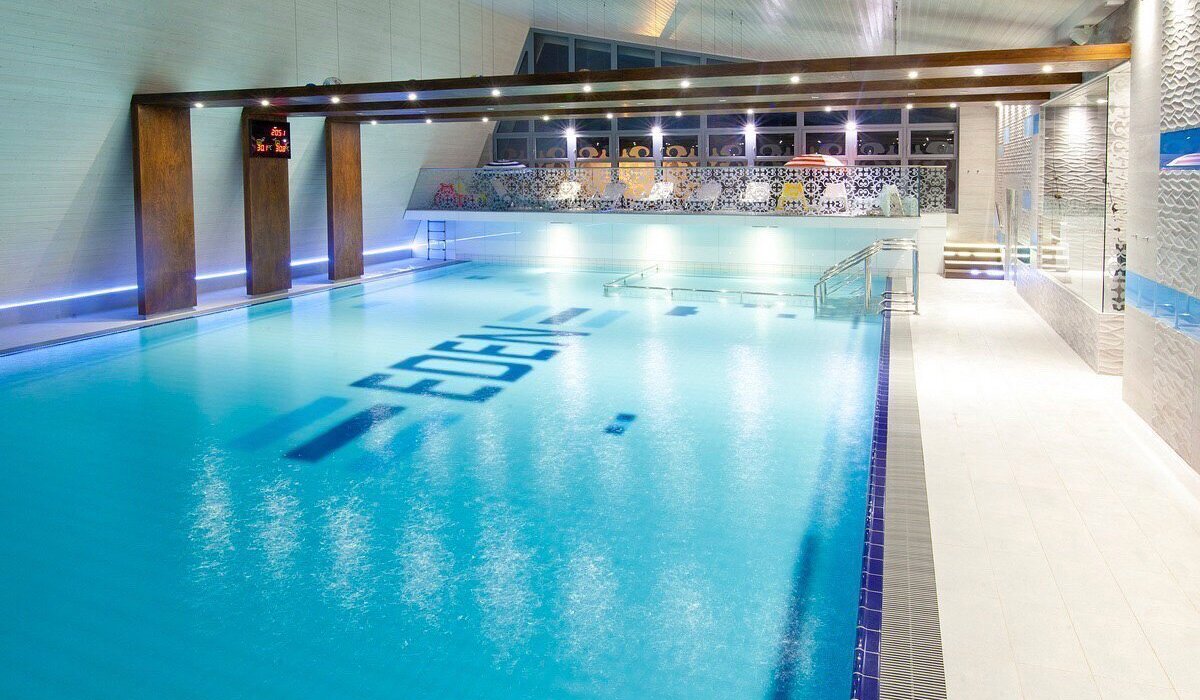 Indoor, well-lit hotel pool with loungers on a mezzanine, stairs and steel handrails