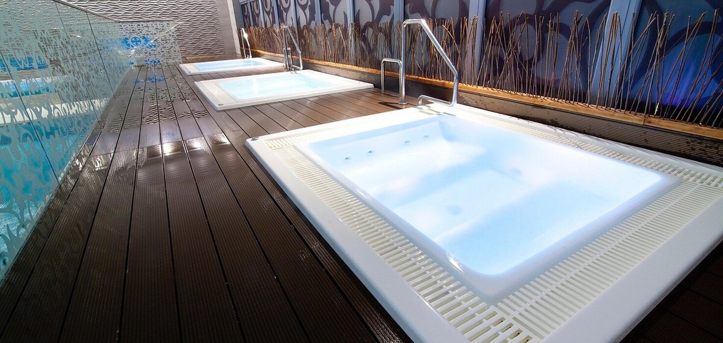 Three illuminated jacuzzis in the spa area on a wooden terrace, a glass wall and a decorative wall with mood lighting