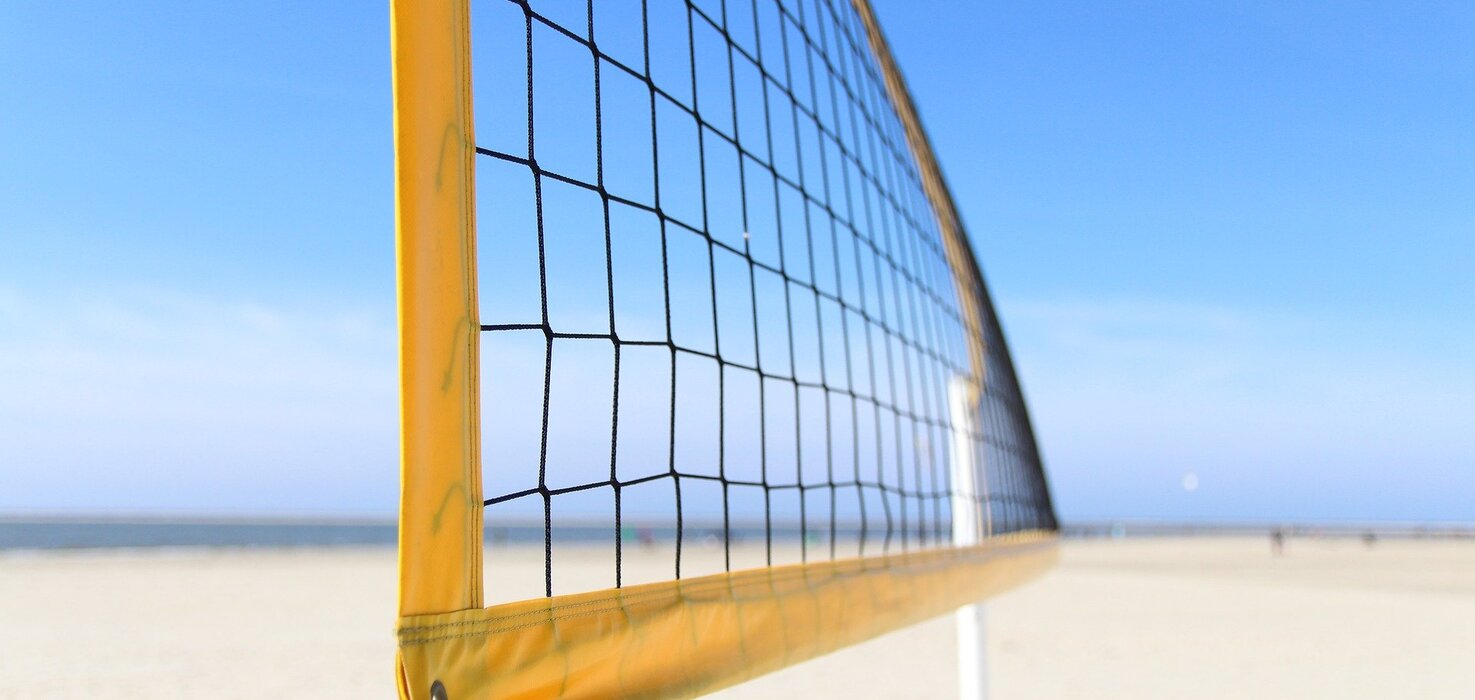 A beach volleyball net on a sandy beach, view of the sea and a cloudless, sunny sky.