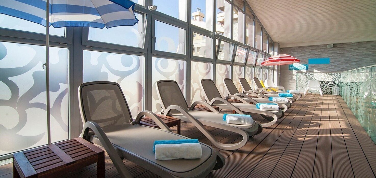Hotel relaxation area with a row of modern loungers, rolled towels, umbrellas and a glass wall