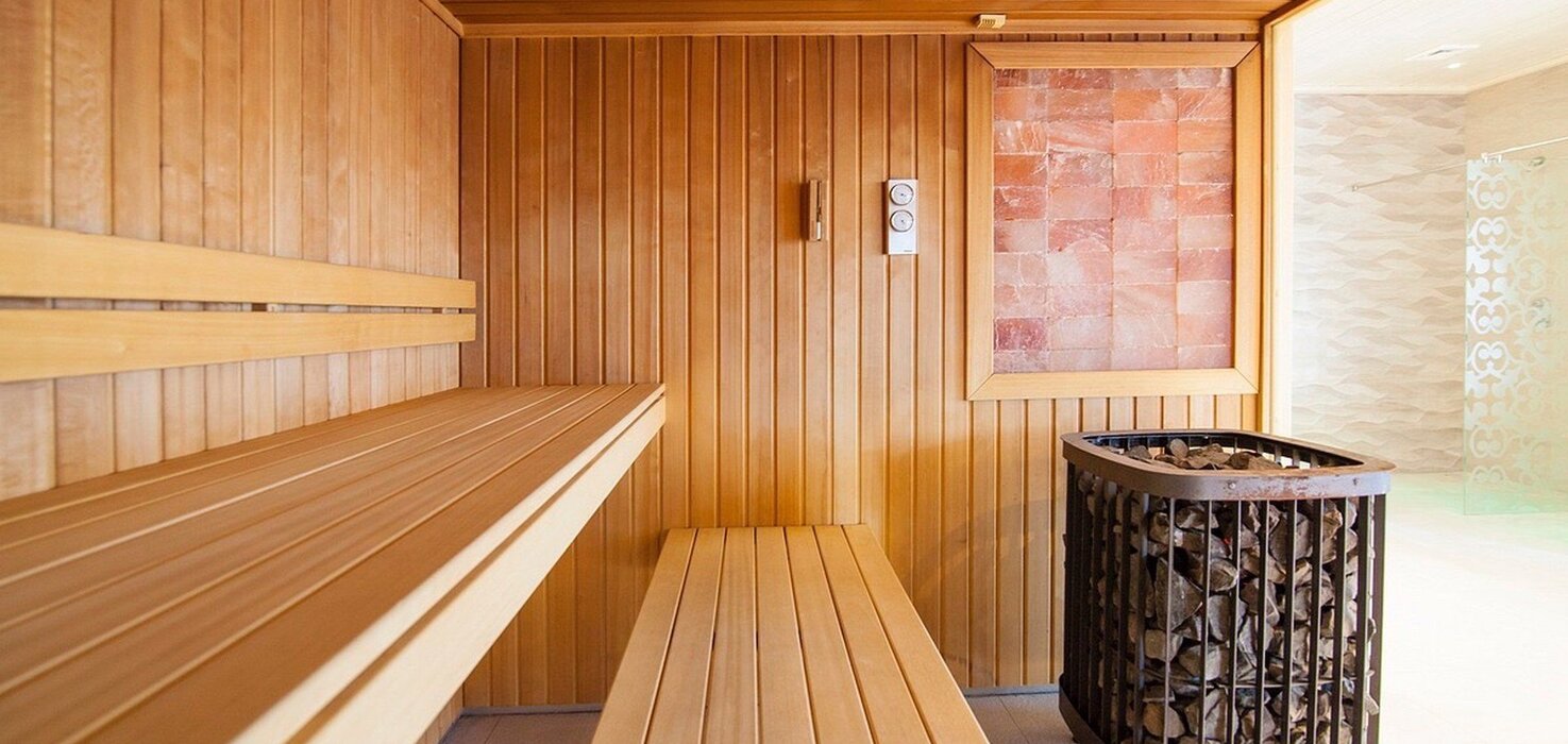 Hotel sauna with light wooden benches, a stone stove and a Himalayan salt wall panel, entrance to the spa.