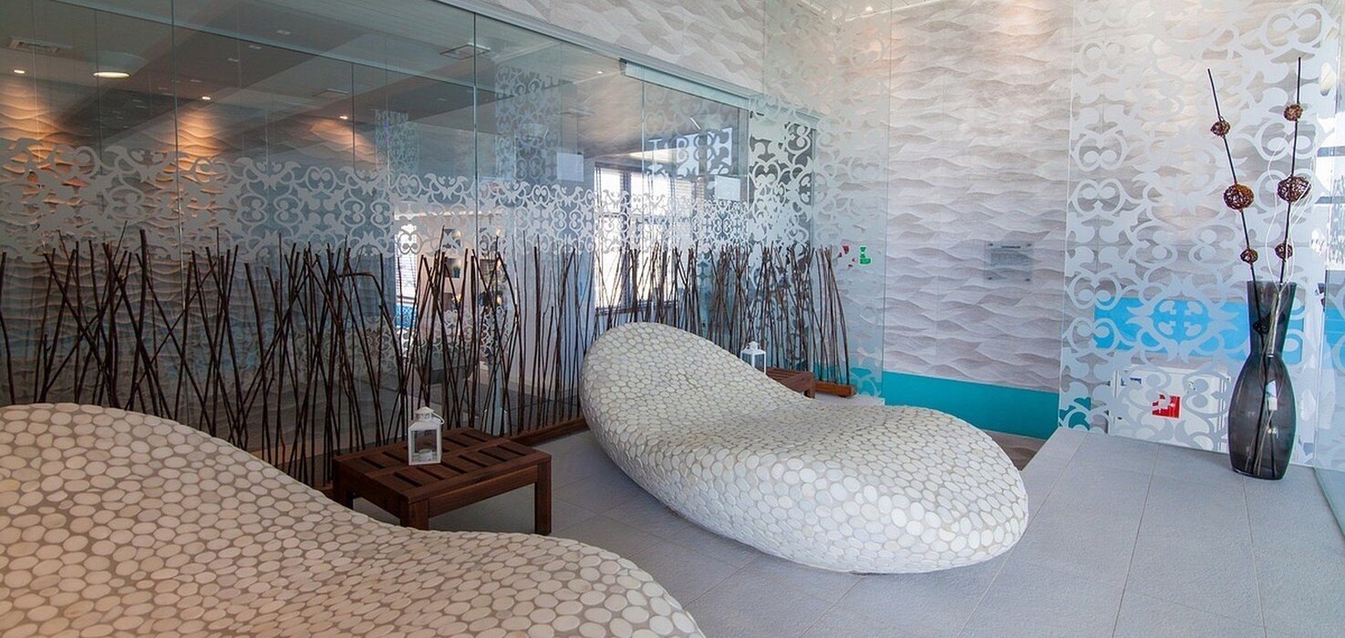 Spa room with two stone-patterned loungers, glass partitions with ornaments, wooden tables and decorative sticks