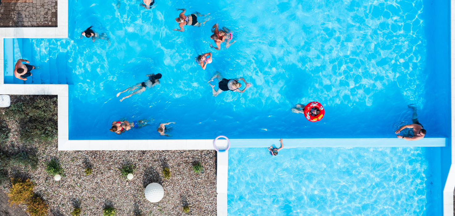 Hotel complex of two pools with light-blue water, families swimming, stone paving with a flower bed