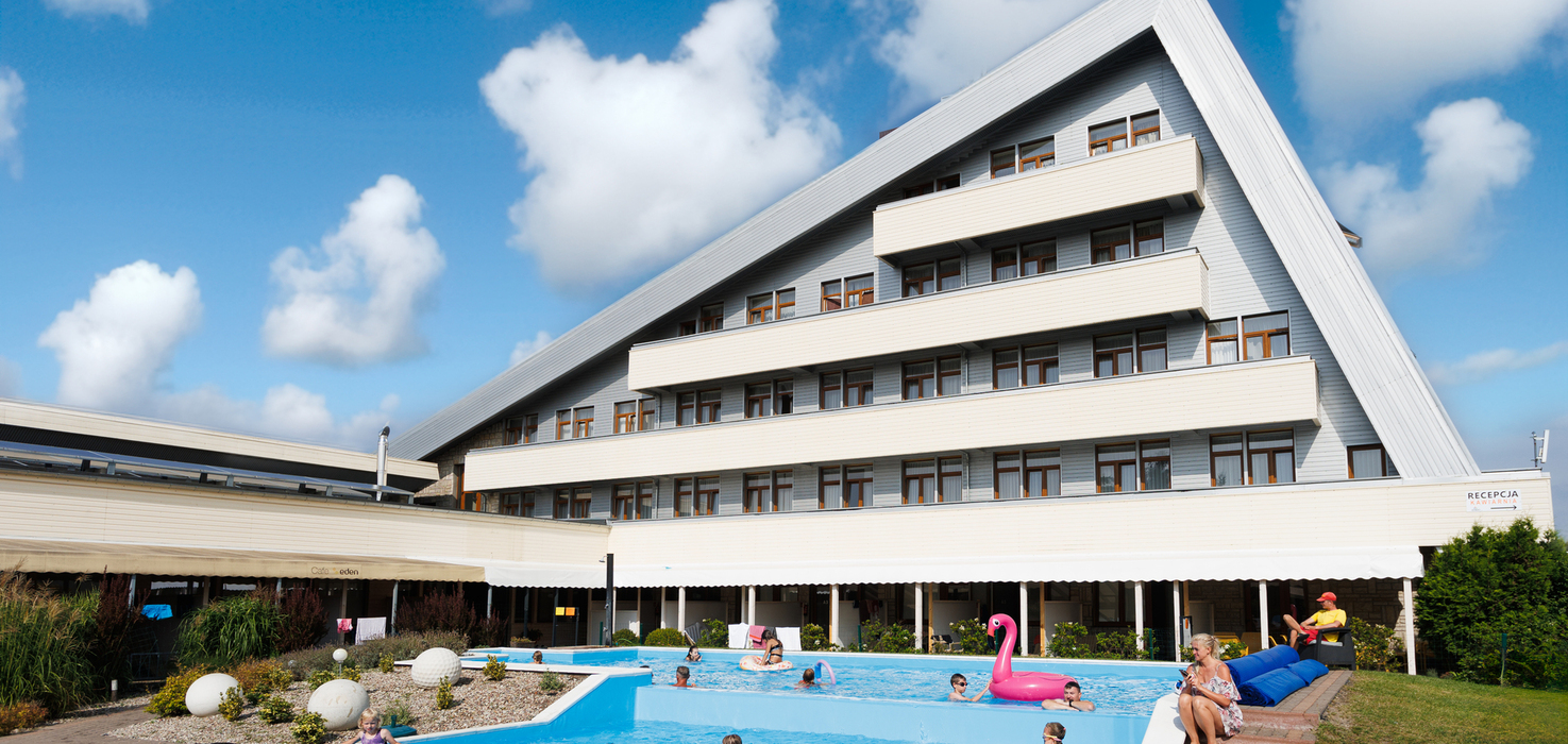 Hotel with a slanted roof and terraced balconies, outdoor pools with families, an inflatable flamingo and loungers.