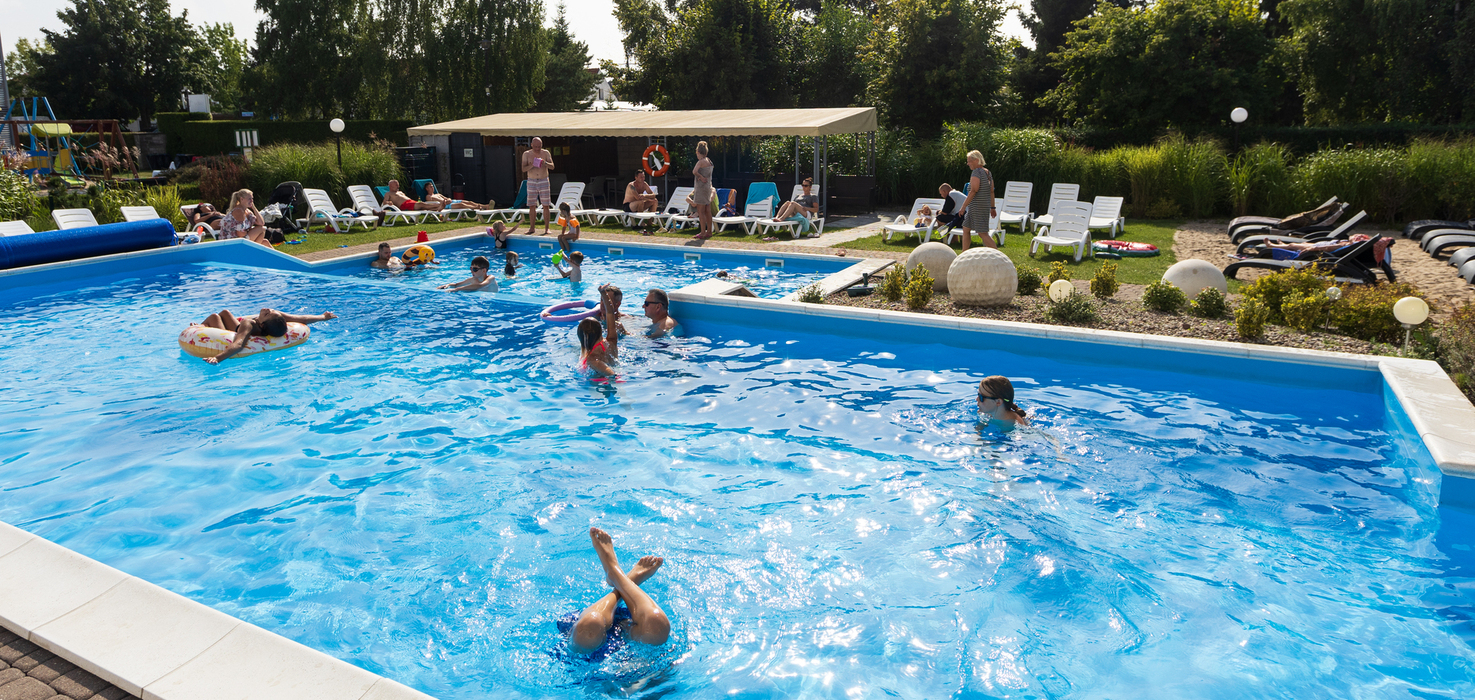 Hotel outdoor pool with loungers, a shaded shelter and families swimming with inflatable toys.