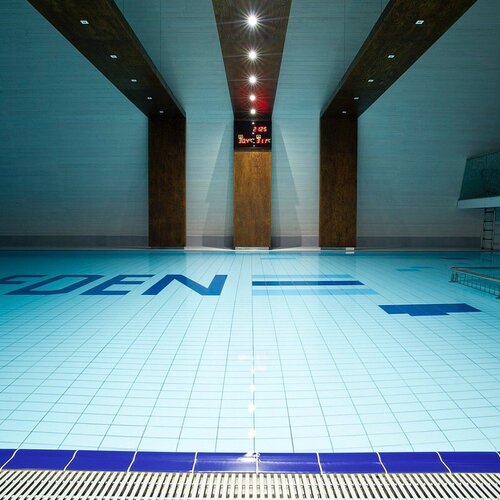 Indoor hotel pool with light tiles, a handrail and steps, wooden beams and a display, relaxing atmosphere