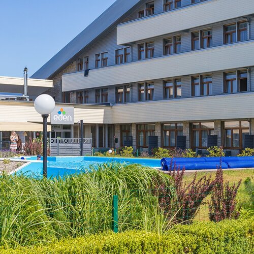 Hotel Eden — outdoor pool, café terrace, loungers and a carefully maintained garden by a modern building.