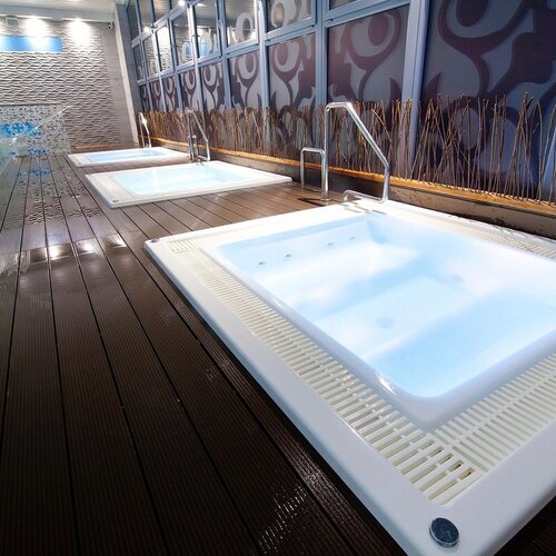 Three illuminated jacuzzis in the spa area on a wooden terrace, a glass wall and a decorative wall with mood lighting