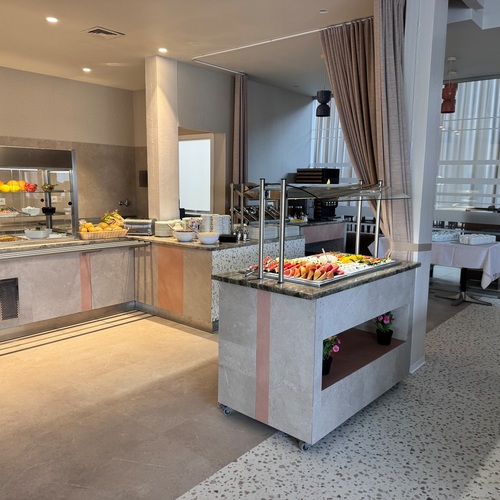 Modern breakfast buffet with displayed fruits, bread, a salad station, a coffee machine and an elegant dining area.