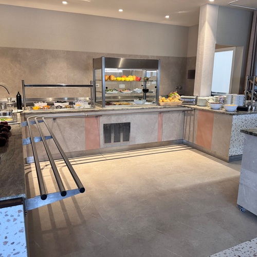 Breakfast buffet with marble counters, displays of fresh fruit, a bread basket, plates and stainless steel covers.